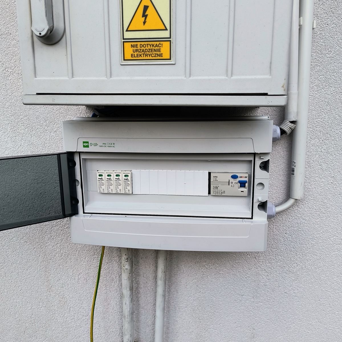 Zamontowana na elewacji rozdzielnica elektryczna z tabliczką ostrzegawczą